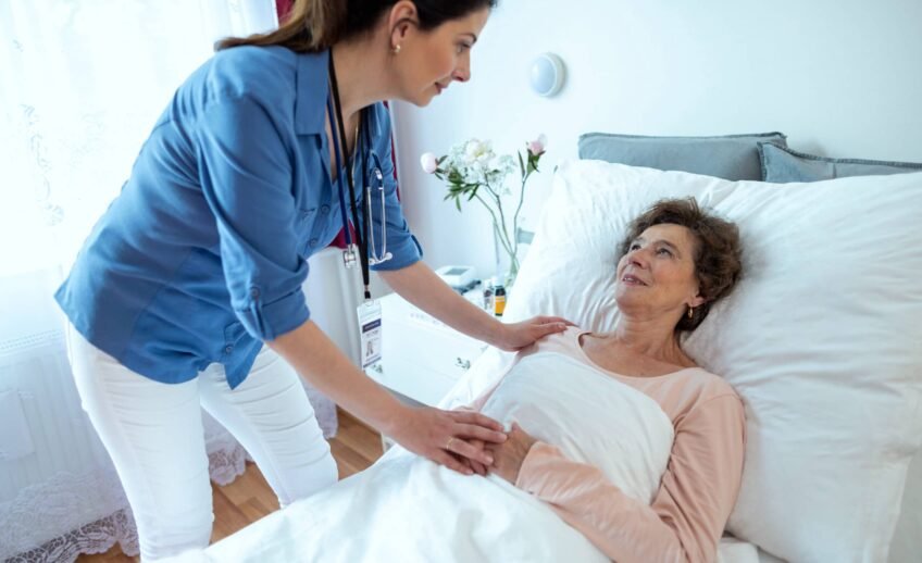 nurse-leaning-over-elderly-woman-lying-in-hospital-2021-08-30-01-20-41-utc-scaled